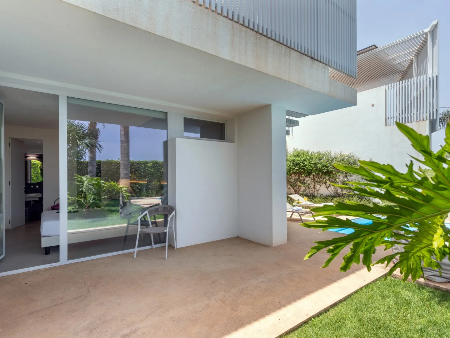A modern patio beside large windows overlooks a landscaped garden and swimming pool.