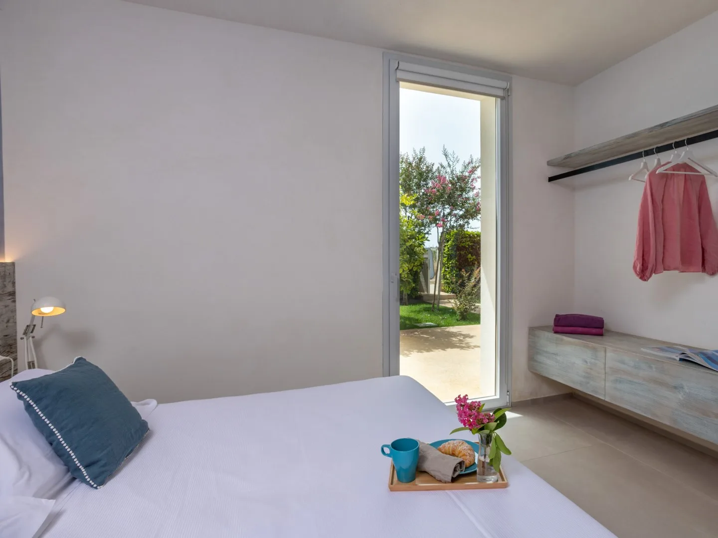 A bedroom with a bed beside a tall window overlooking a garden.