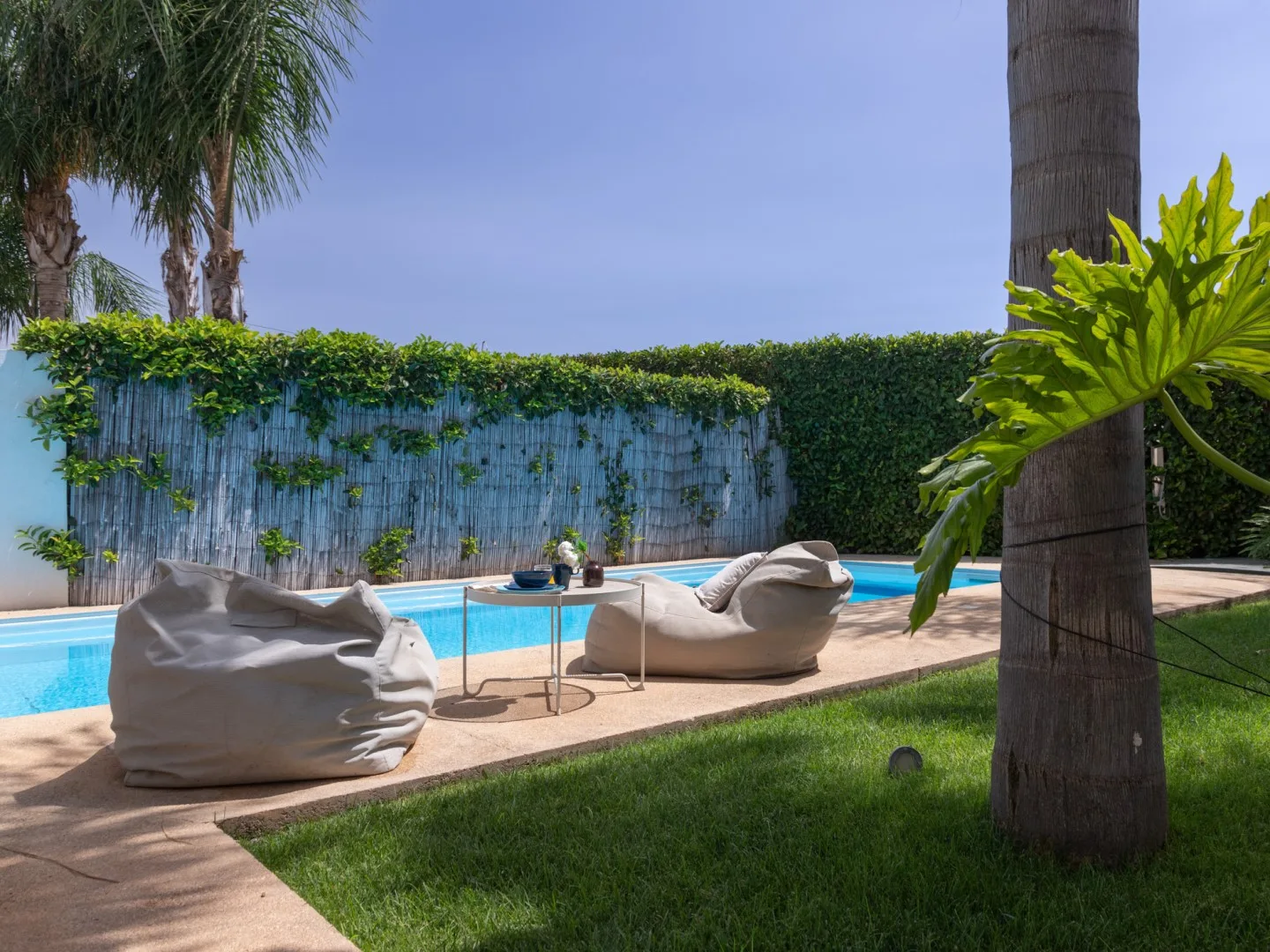 A landscaped swimming pool area with casual outdoor seating and greenery.
