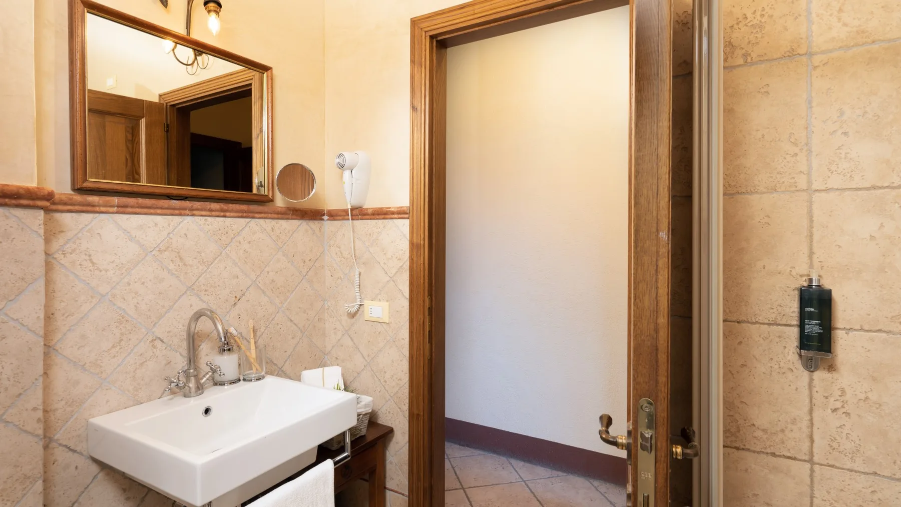 Un baño alicatado con un lavabo blanco y una puerta abierta.