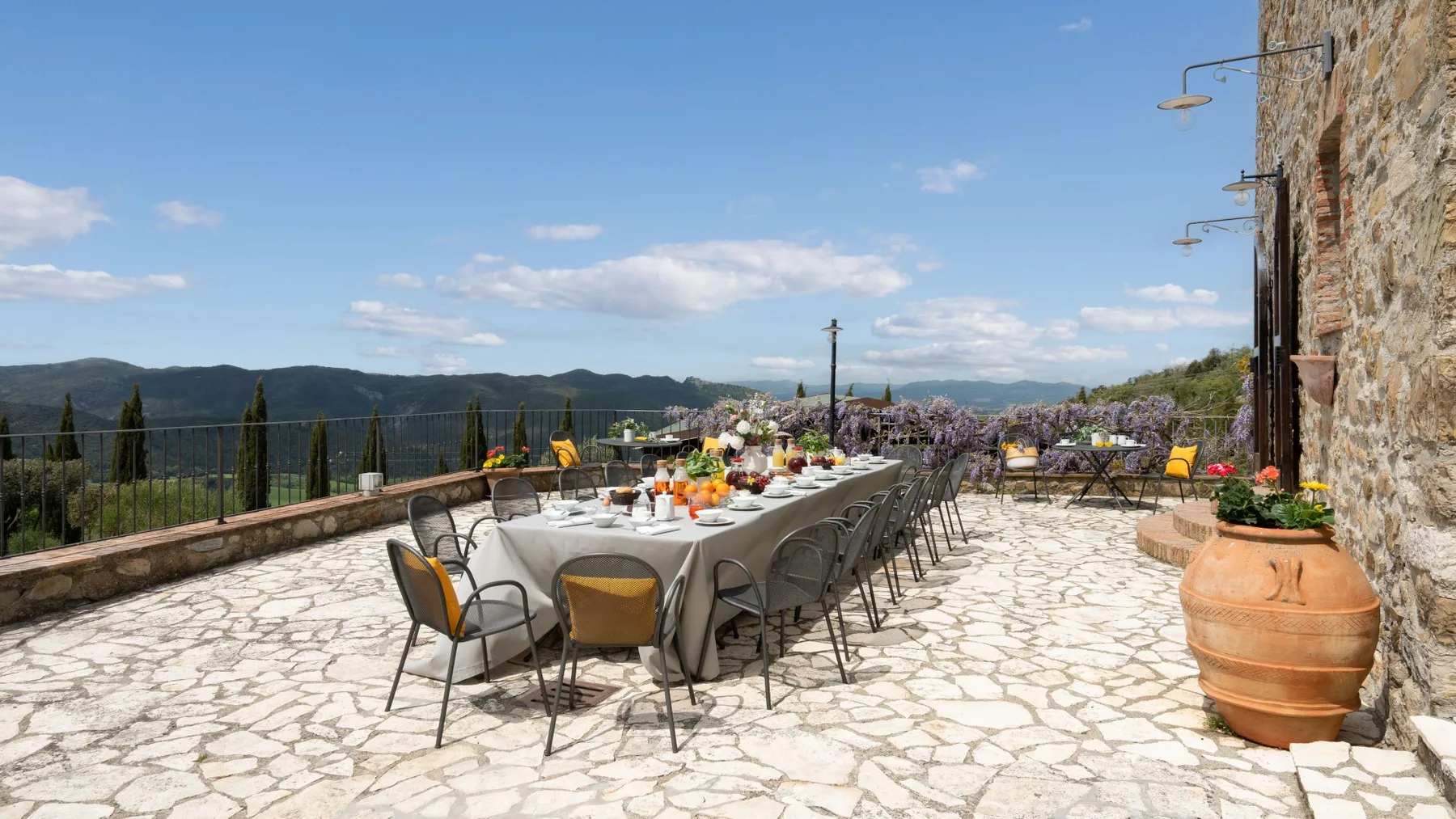 Una terraza de piedra tiene una larga mesa al aire libre con vistas a las montañas.