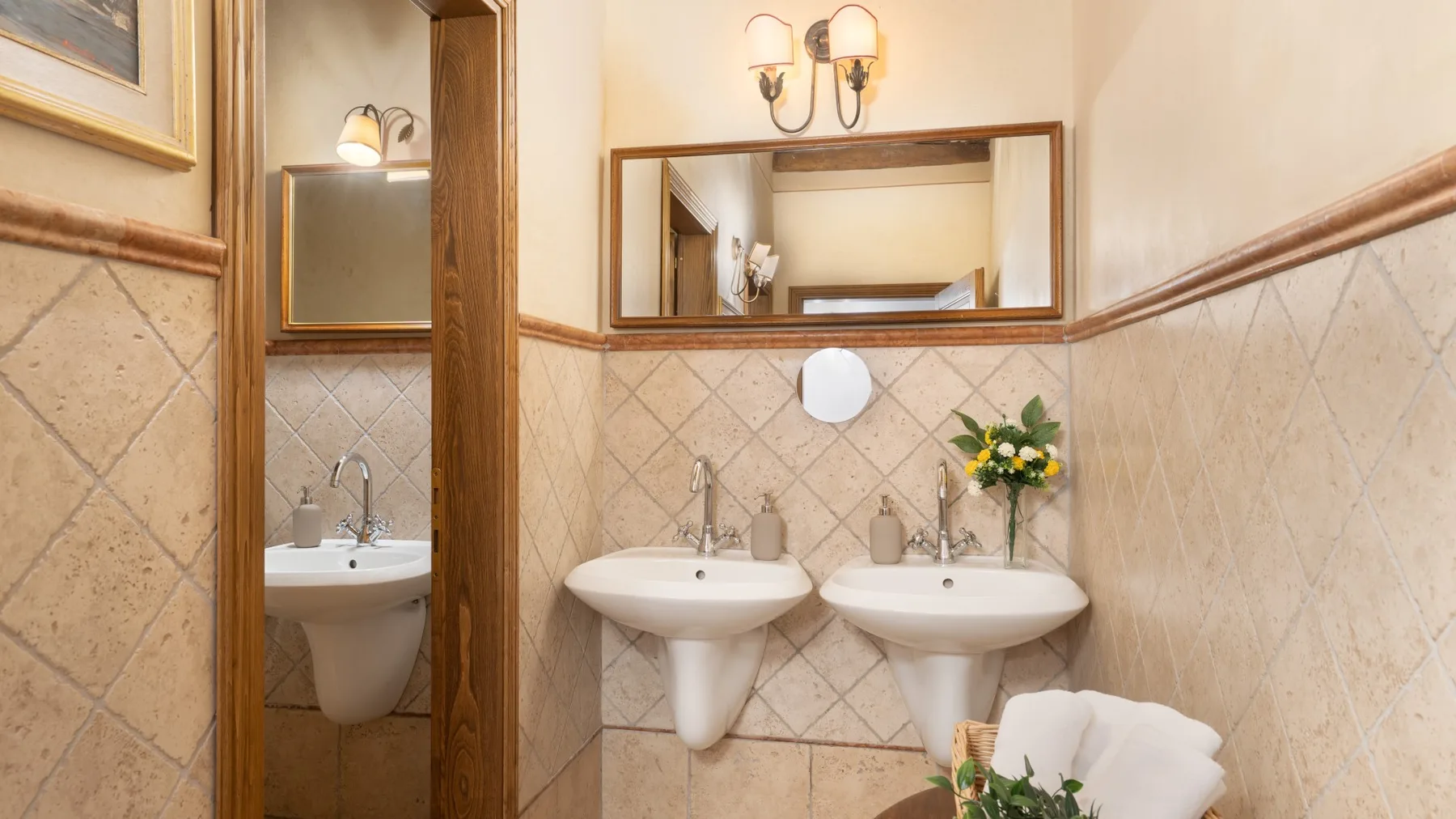 Un baño con dos lavabos, espejos de pared y paredes de azulejos beige.