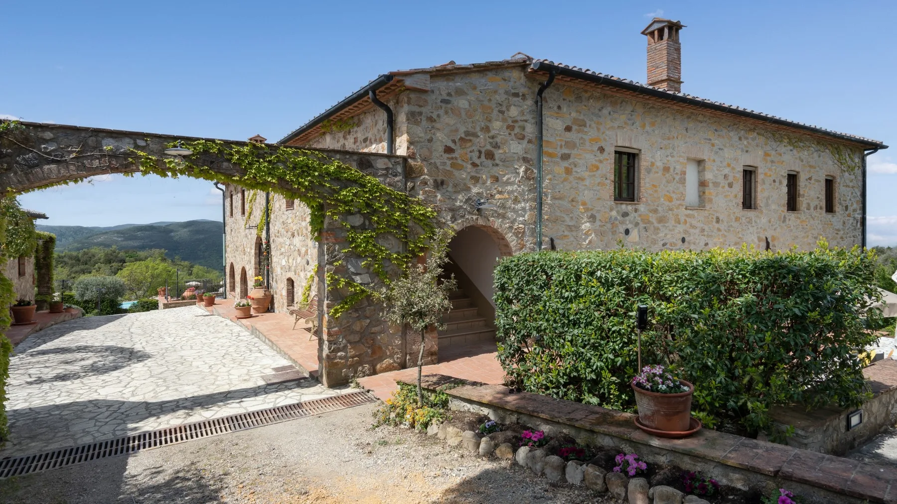 Un edificio de piedra junto a un patio pavimentado, con vegetación junto a la entrada.