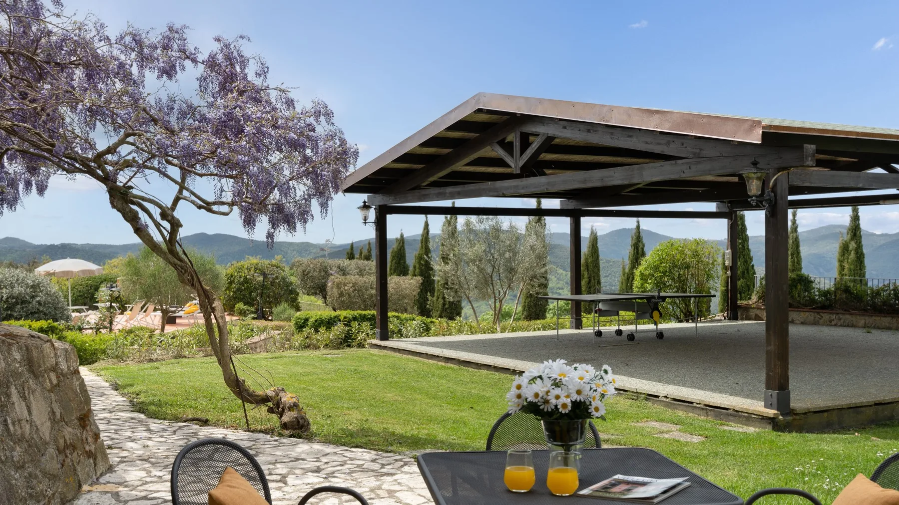 Una zona de estar al aire libre y cubierta da a un jardín con colinas al fondo.