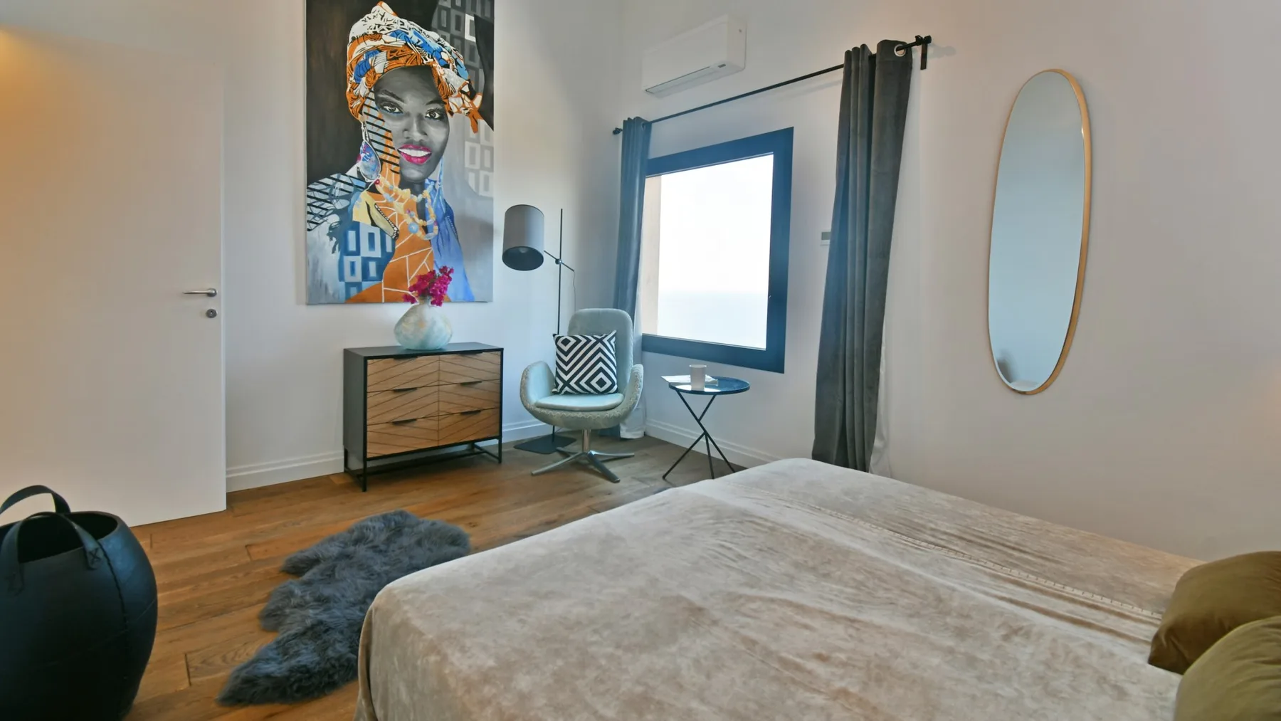 Un dormitorio con un gran retrato, una cómoda de madera, una silla y una cama junto a una ventana alta.