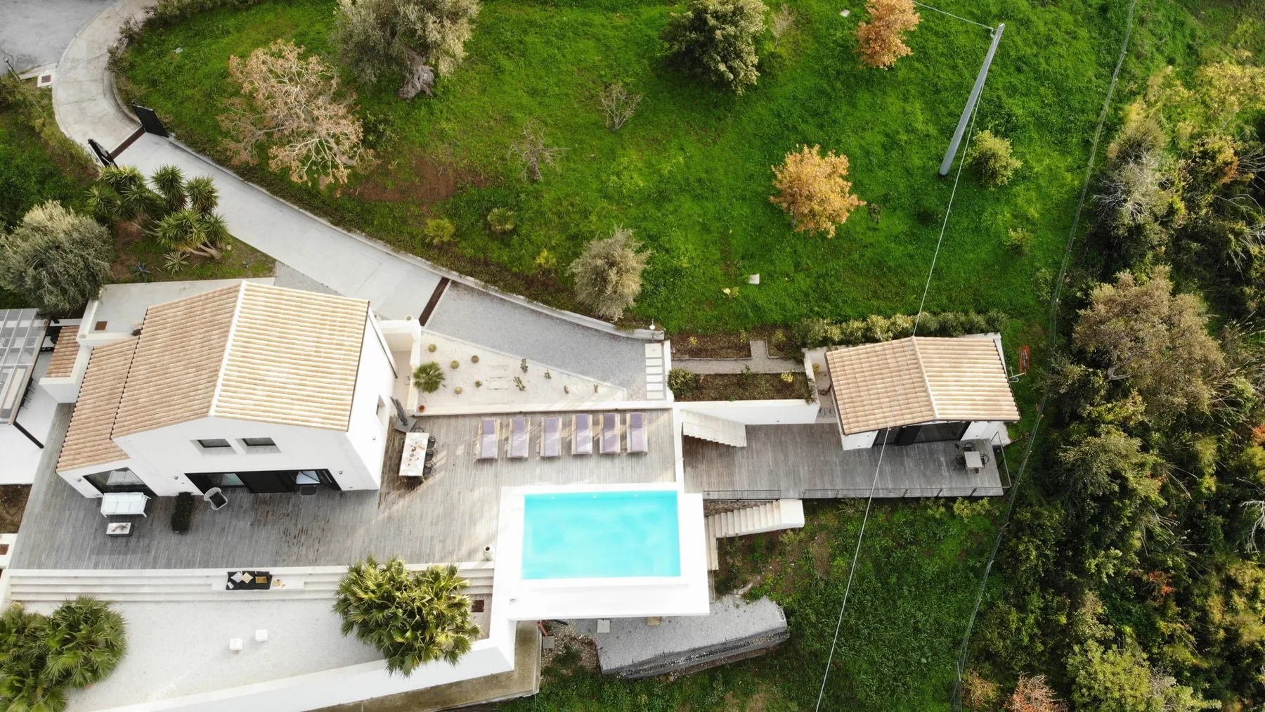 Vista aérea de una casa blanca, una piscina turquesa, patios con baldosas y un jardín verde.