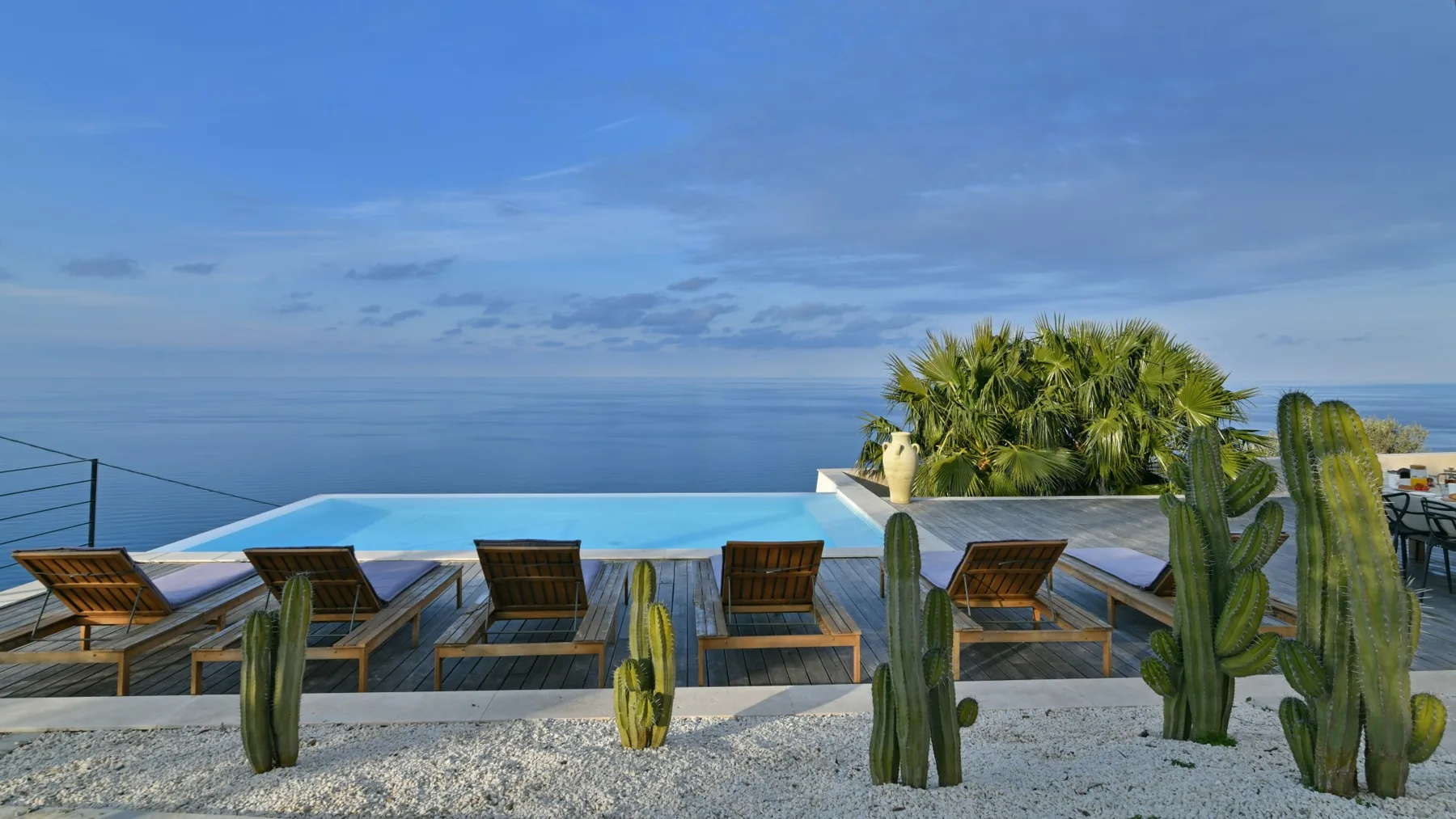 Una terraza en la azotea da al mar, con una piscina estrecha, tumbonas de madera y cactus en primer plano.