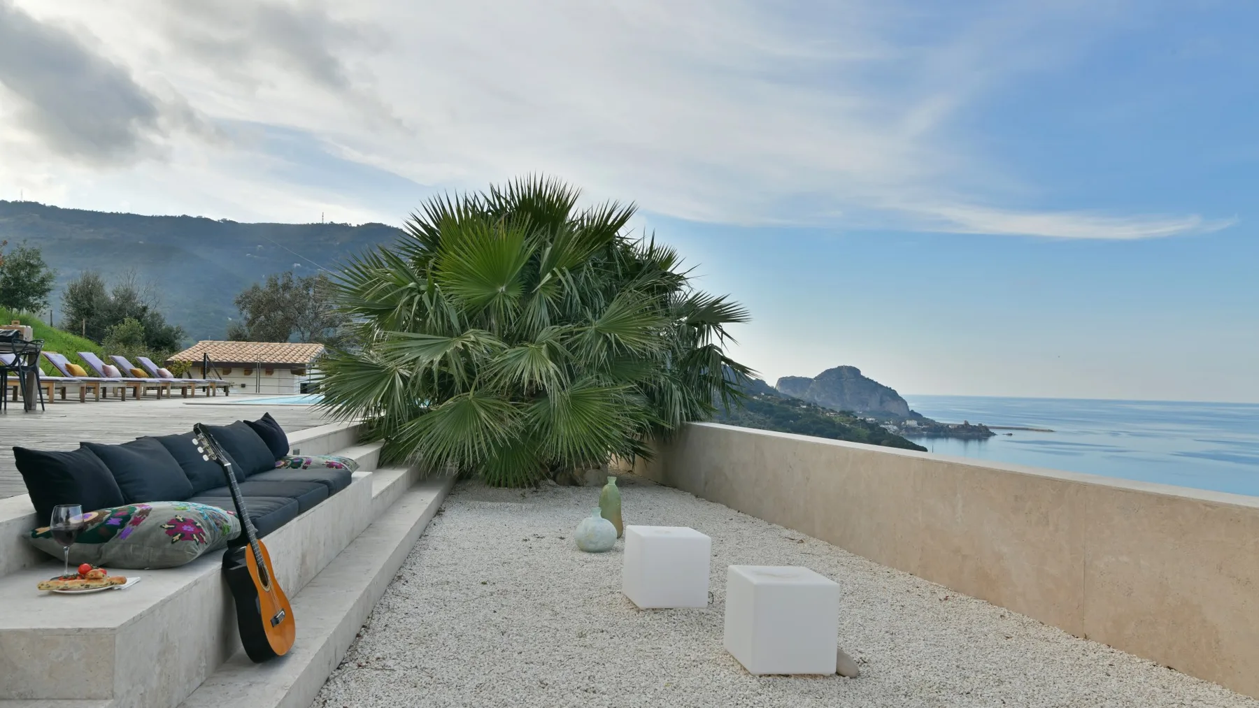 Una terraza de grava tiene asientos empotrados, una palmera abanico y un muro bajo con vistas al agua.