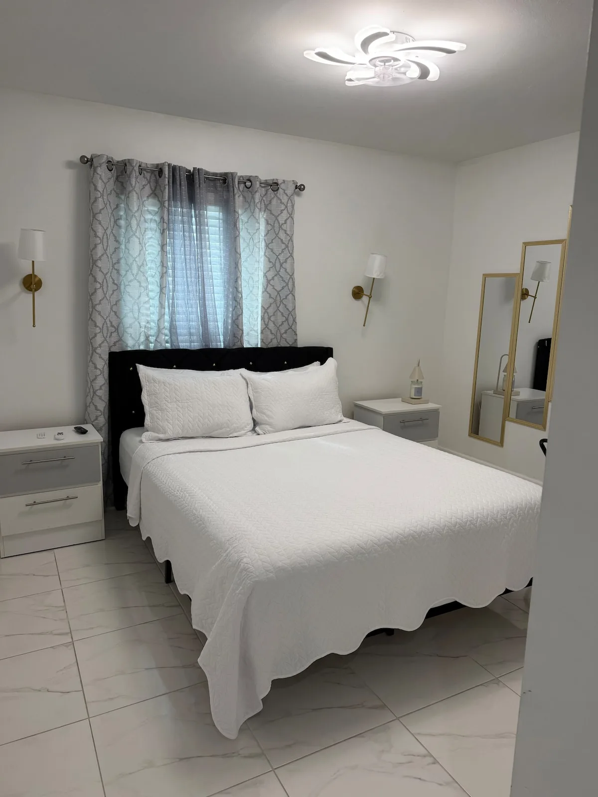 A bedroom with a neatly made bed beneath a window with patterned curtains.