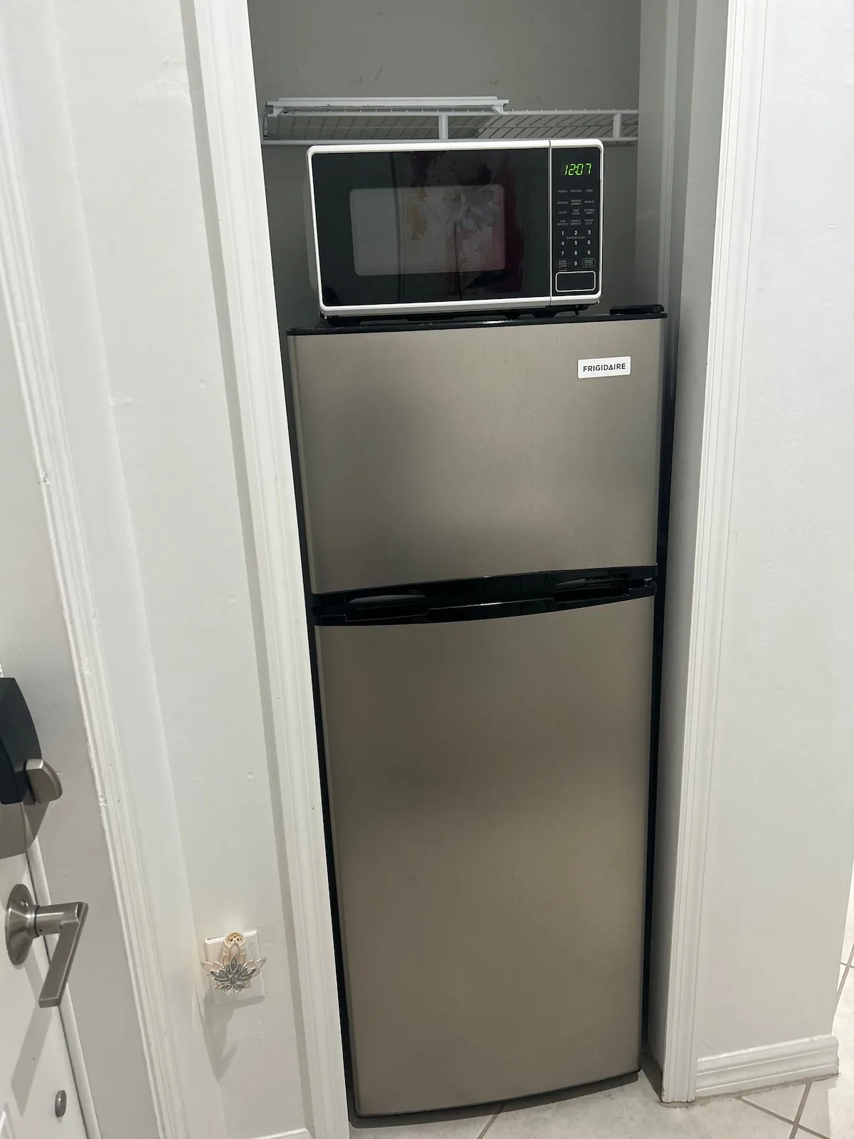 A refrigerator and microwave are set in a narrow kitchen alcove.