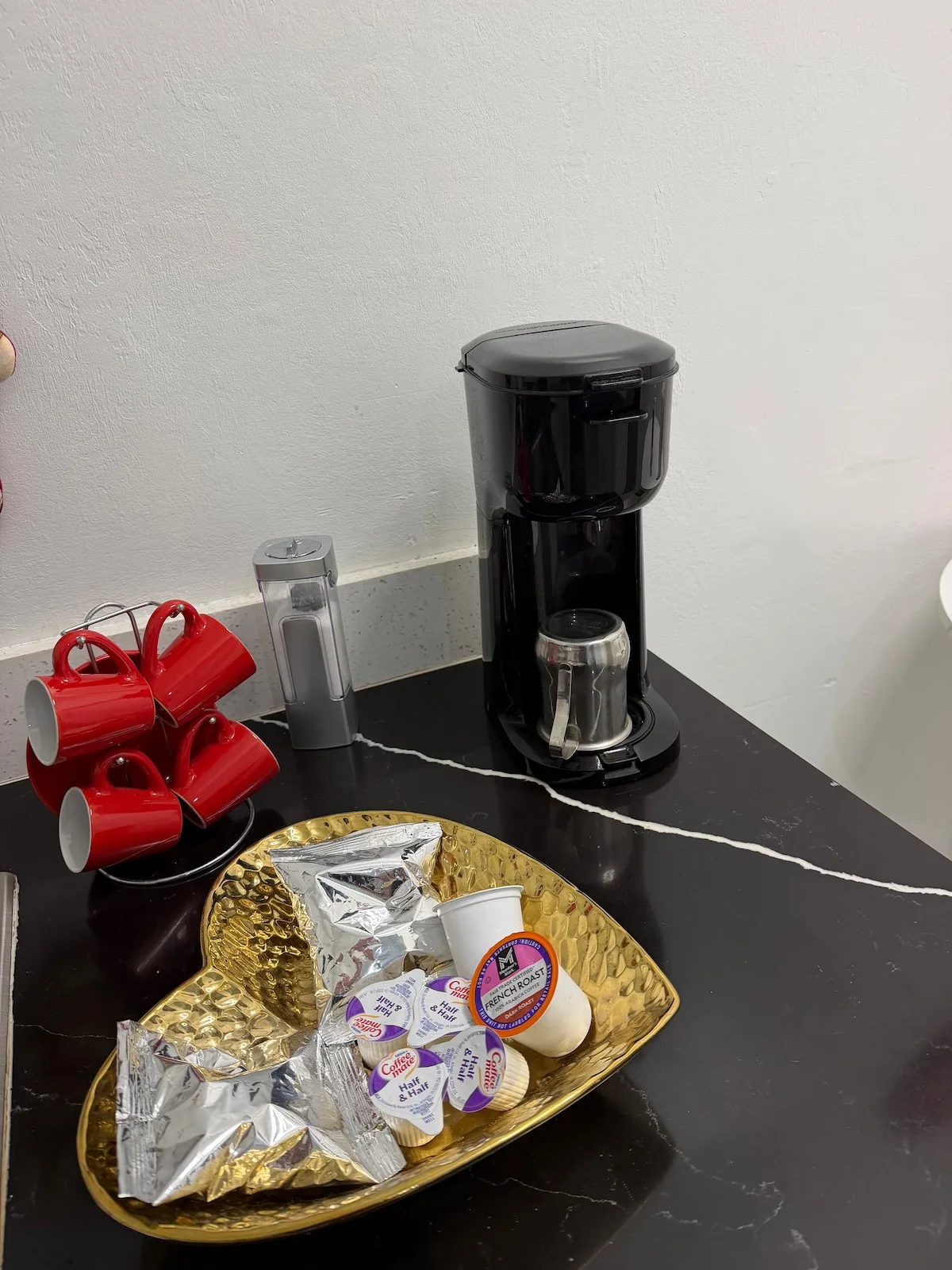 A coffee station with a drip coffee maker, red mugs, and assorted coffee pods.