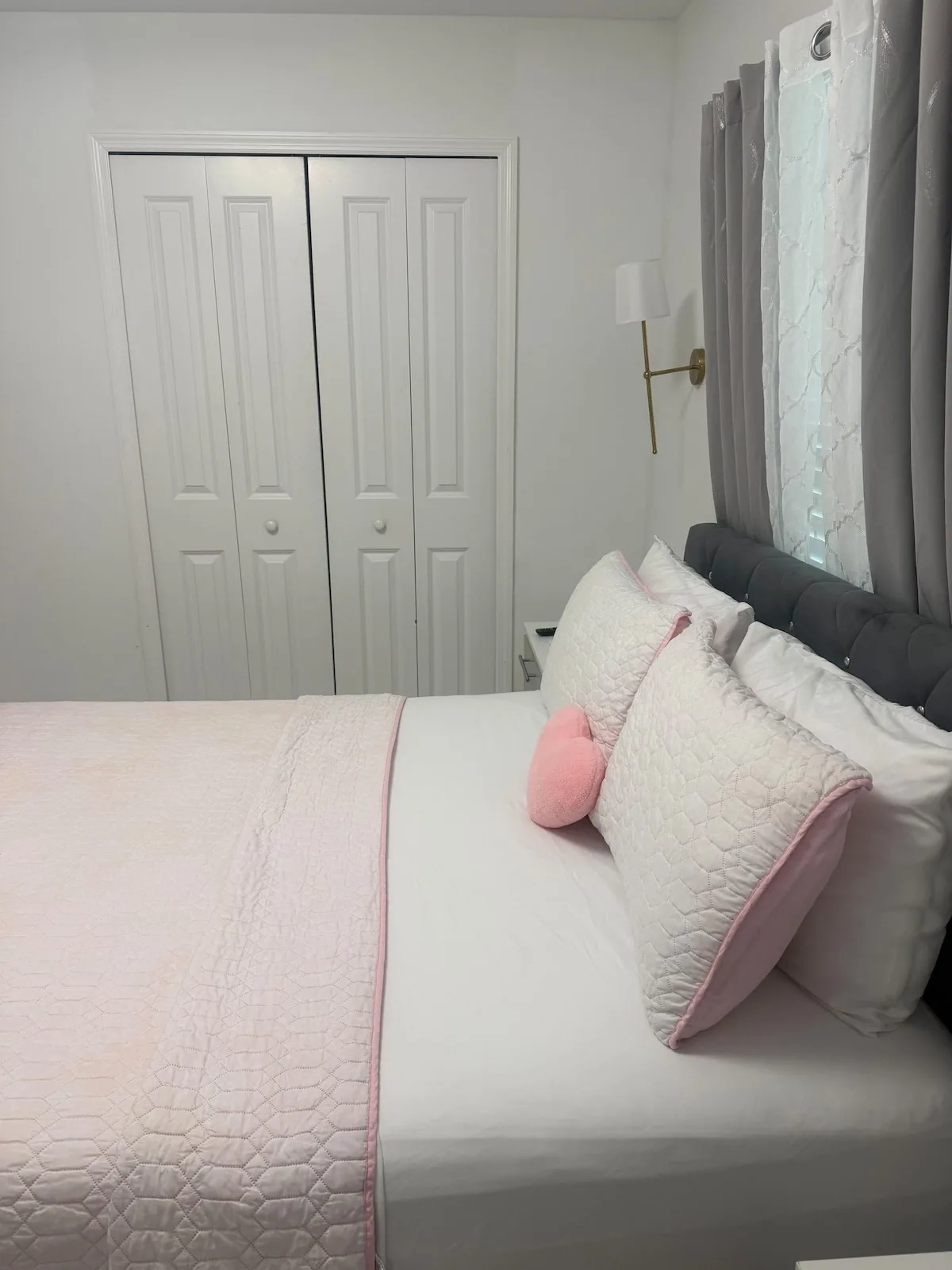A bedroom with a neatly made bed and pale pink bedding.