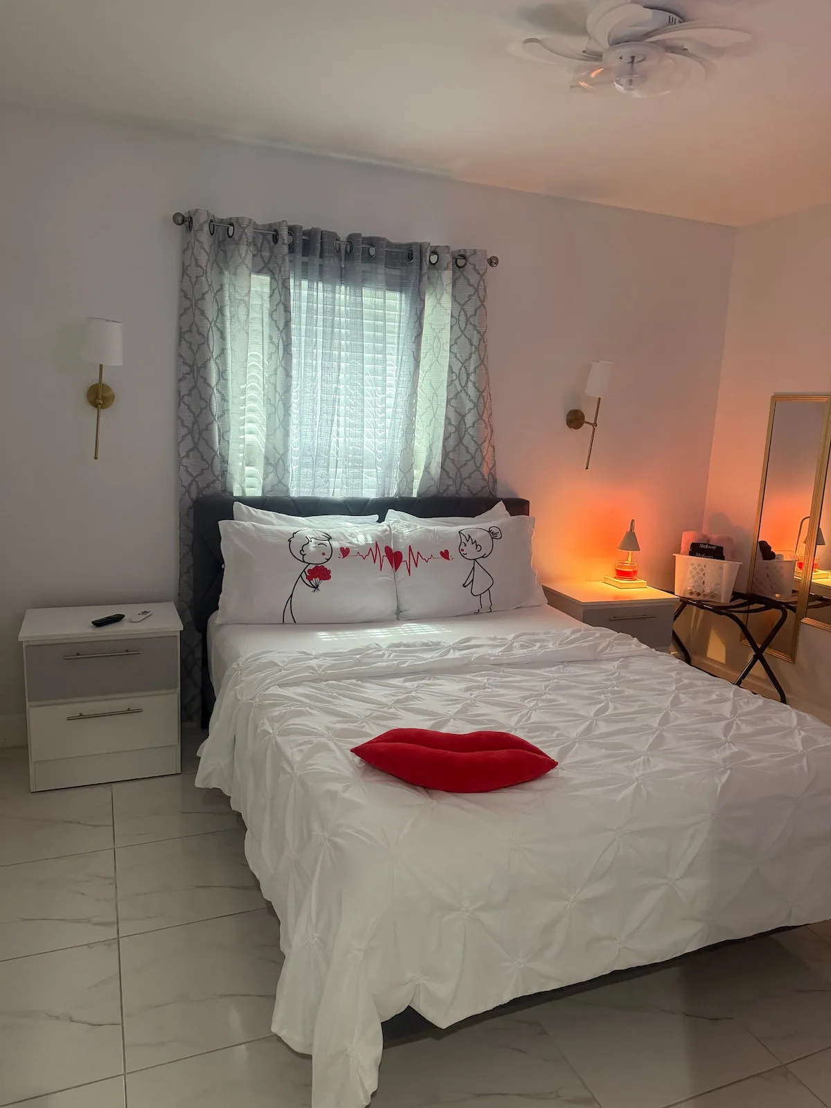 A bedroom with a bed dressed in white bedding and a red cushion.