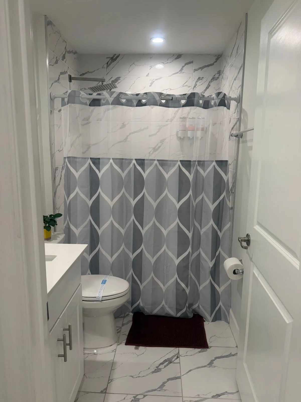 A bathroom with a patterned shower curtain and a sink beside the doorway.
