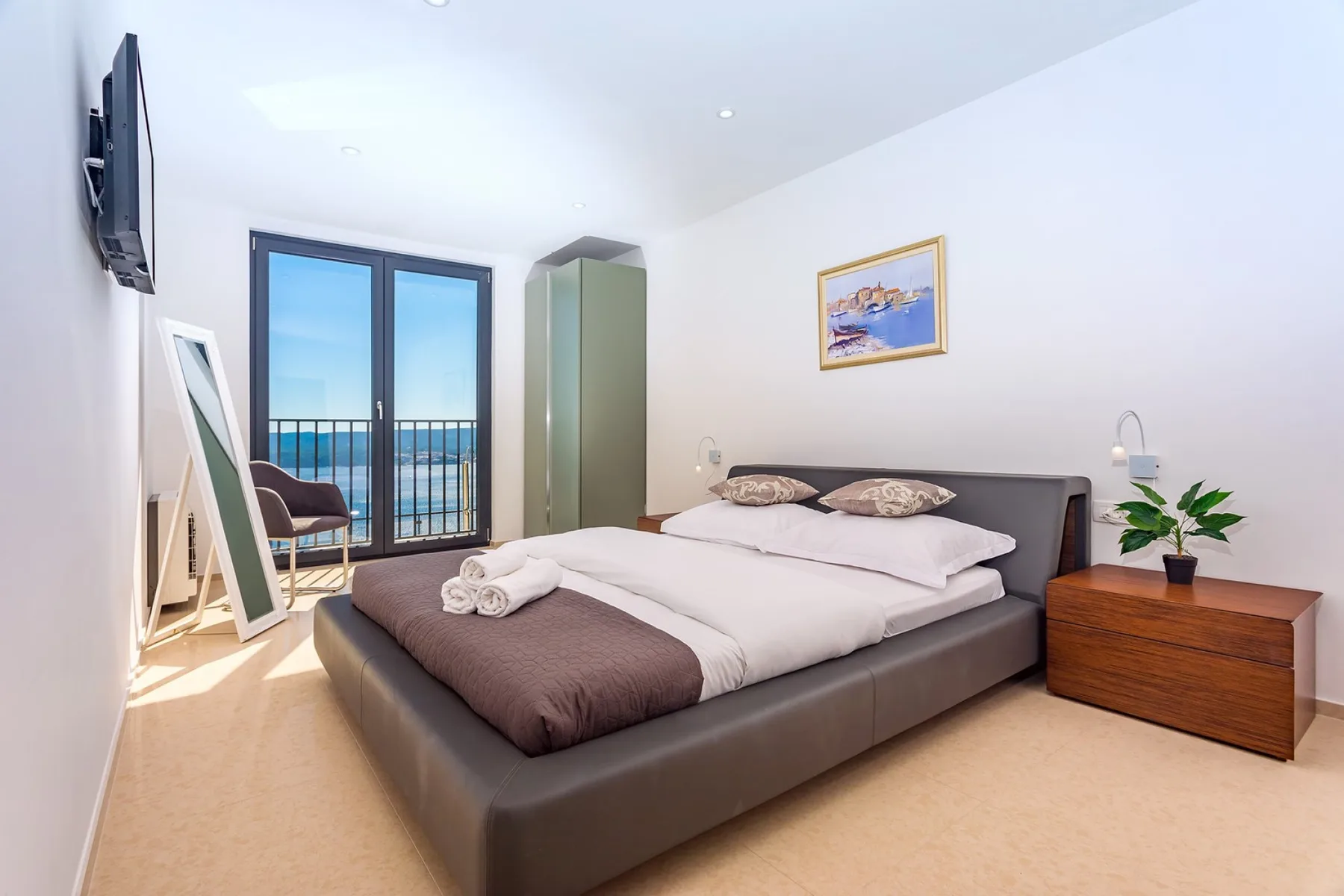 A bright bedroom with a double bed beside glass doors opening onto a balcony.
