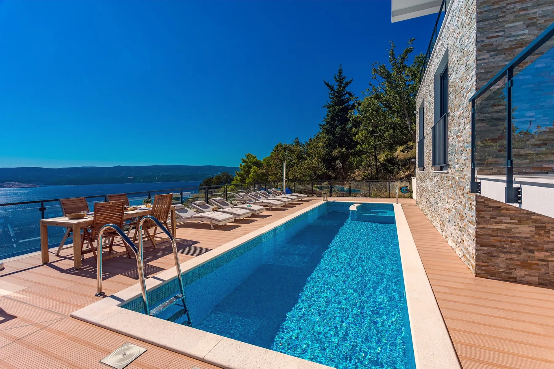 A swimming pool and deck overlook the water beside a stone-faced building.