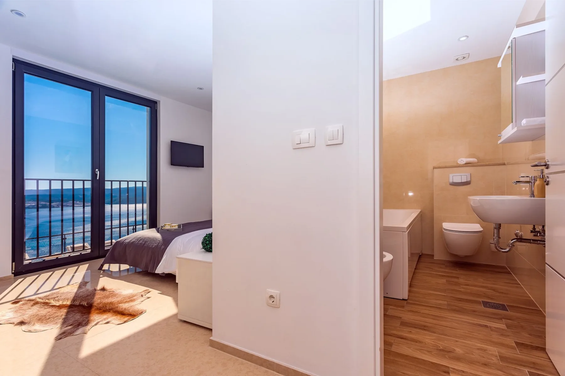 A bedroom with a large window beside a bathroom with a sink and toilet.