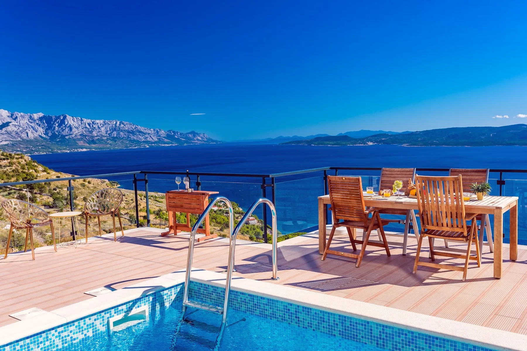 A swimming pool and outdoor dining area overlook the sea and distant mountains.