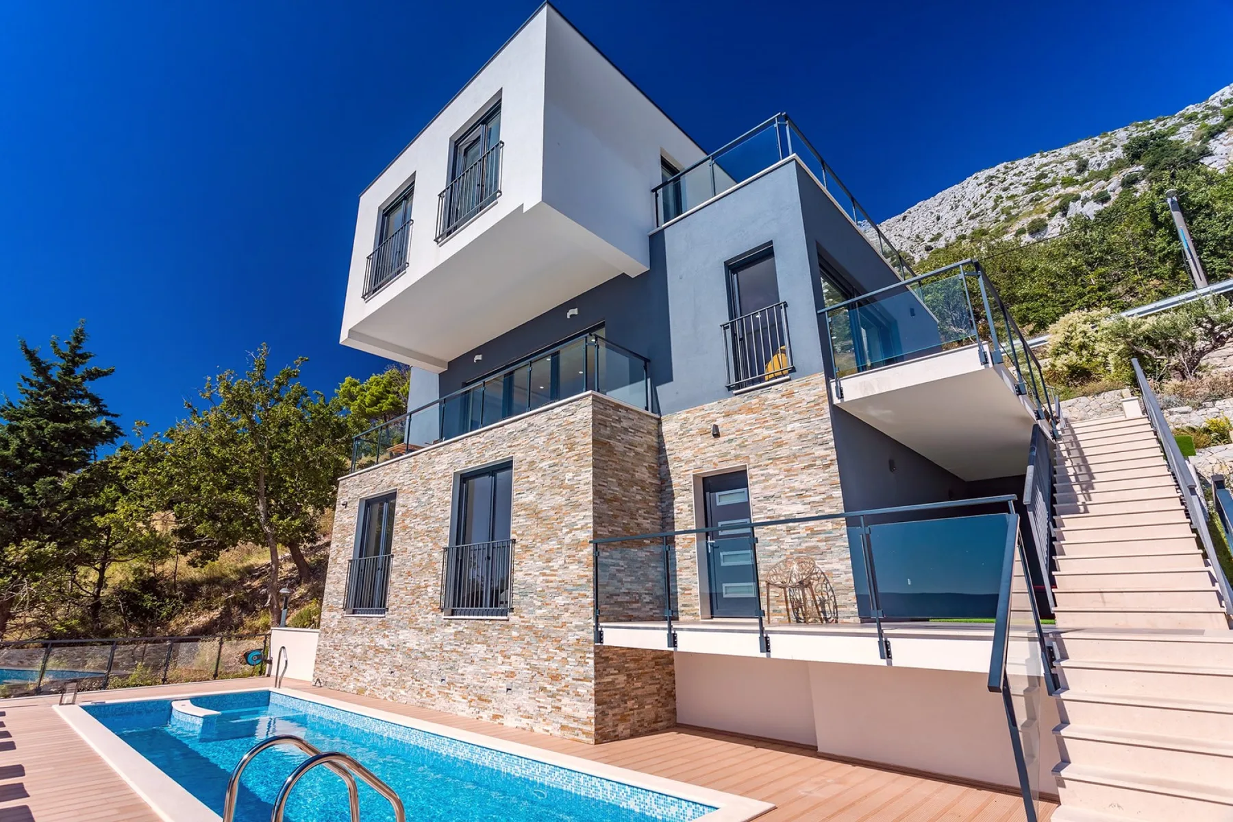 A modern house with stone-clad walls and a swimming pool in front.