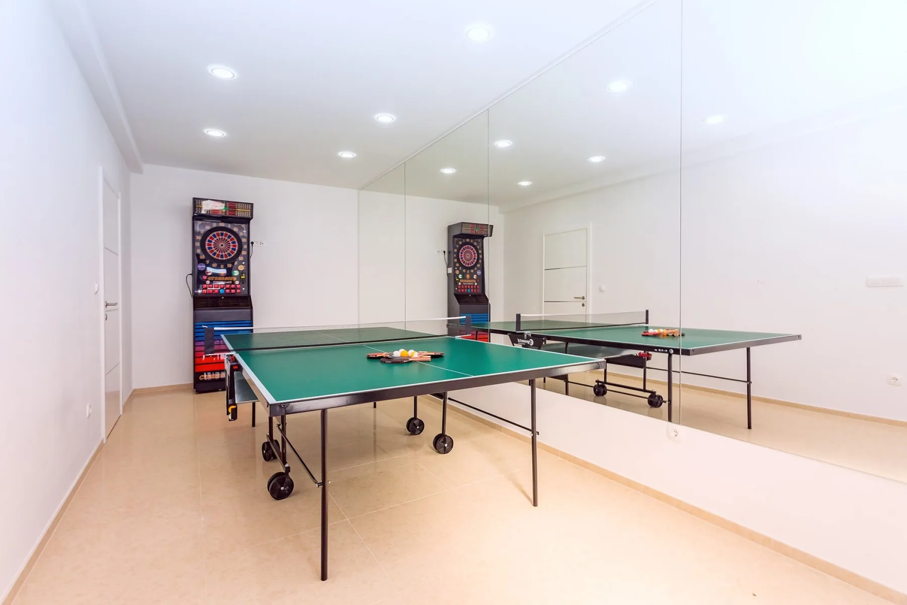 A bright recreation room with a green table tennis table and wall mirrors.