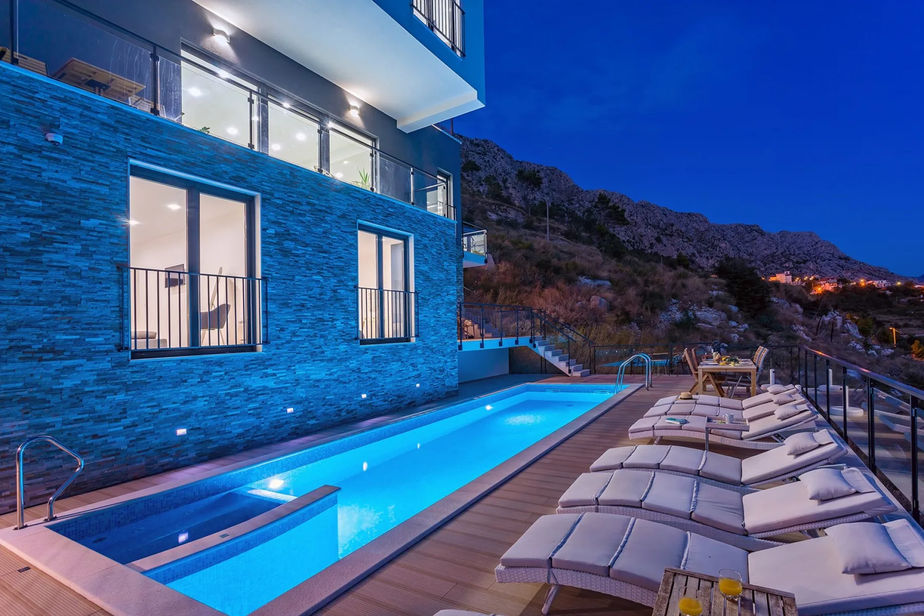 An outdoor swimming pool beside a modern building, with lounge seating along the deck.
