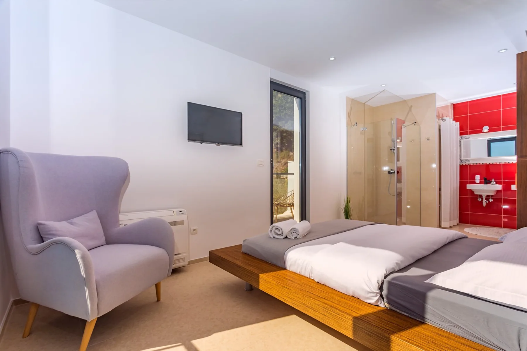 A bedroom with two beds, an armchair, and a glass shower area.