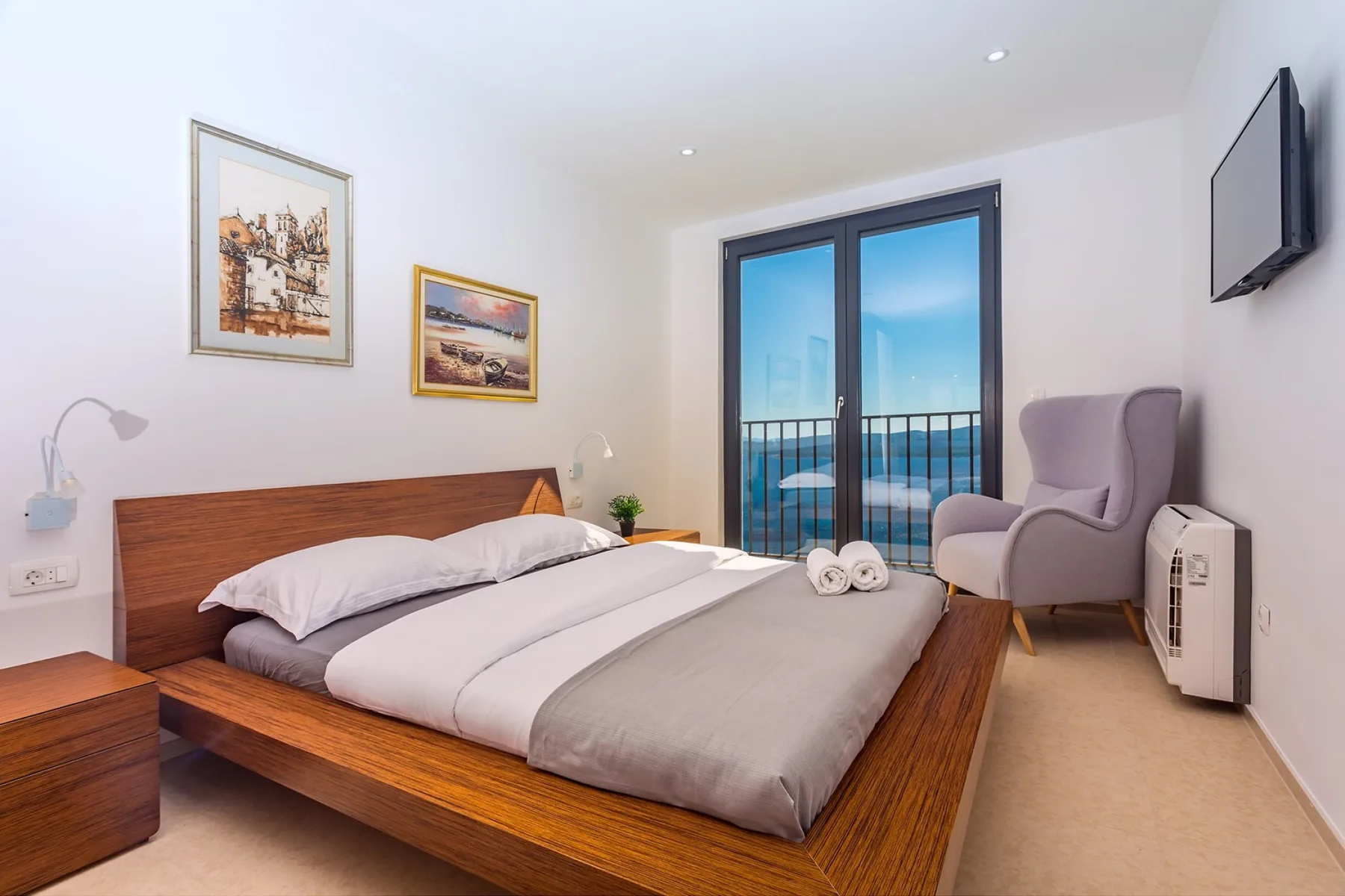 A bedroom with a wooden bed, framed artwork, and glass doors opening onto a balcony.