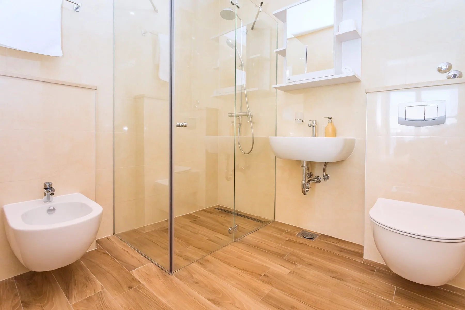 A bright bathroom with a glass shower, wall-mounted sink, and toilet.