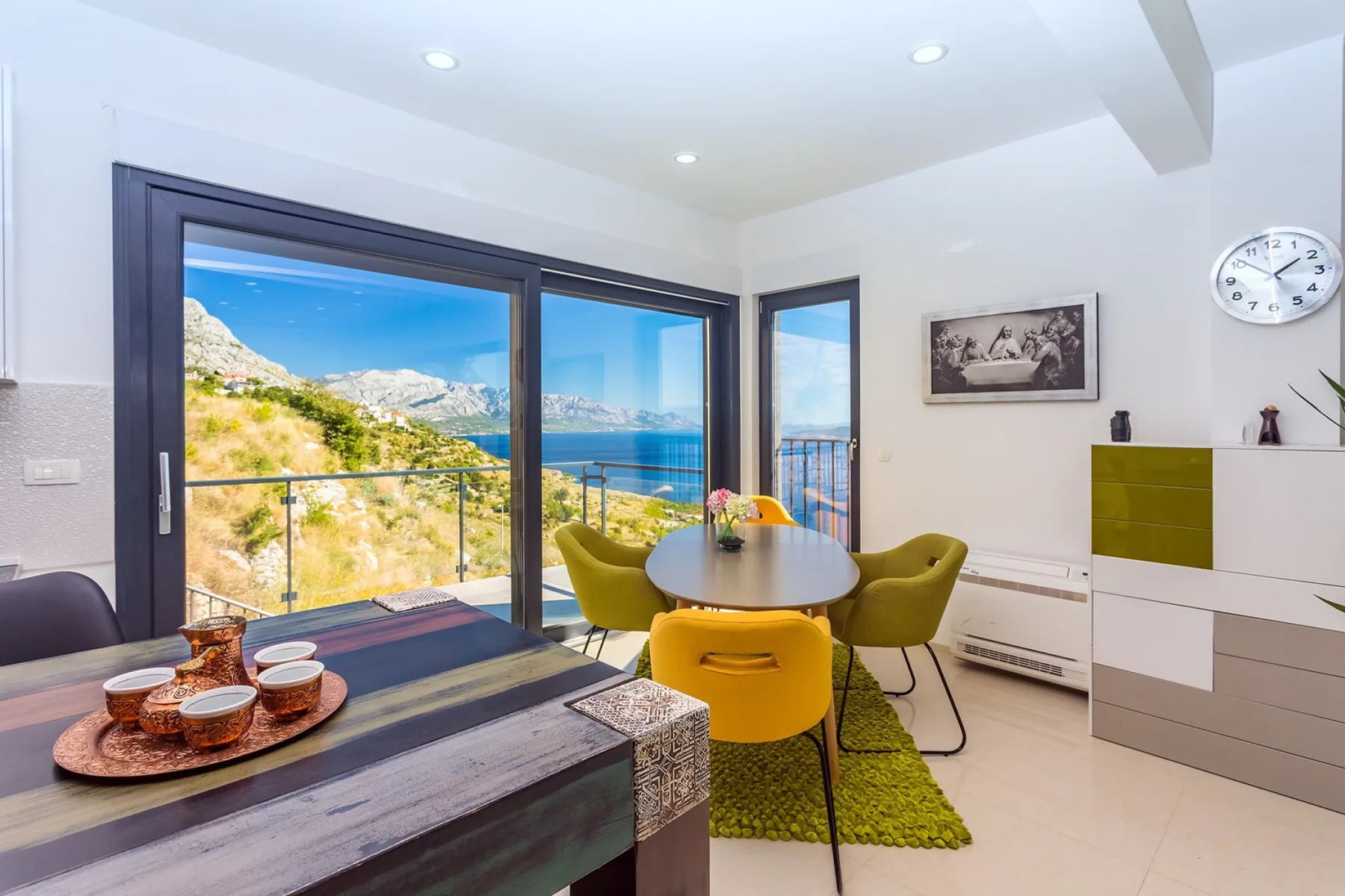A dining area with a table and chairs beside large windows overlooking the sea.