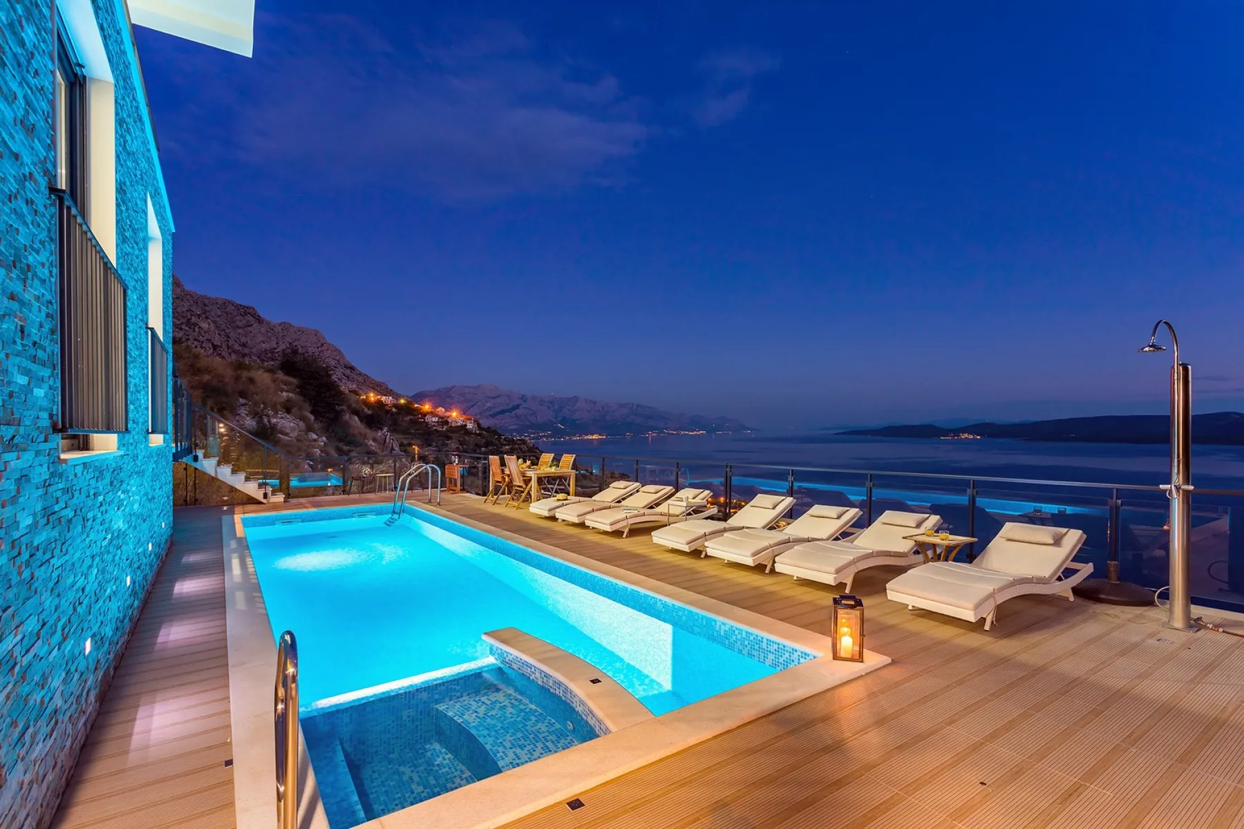 A swimming pool and lounge seating overlook the water at dusk.