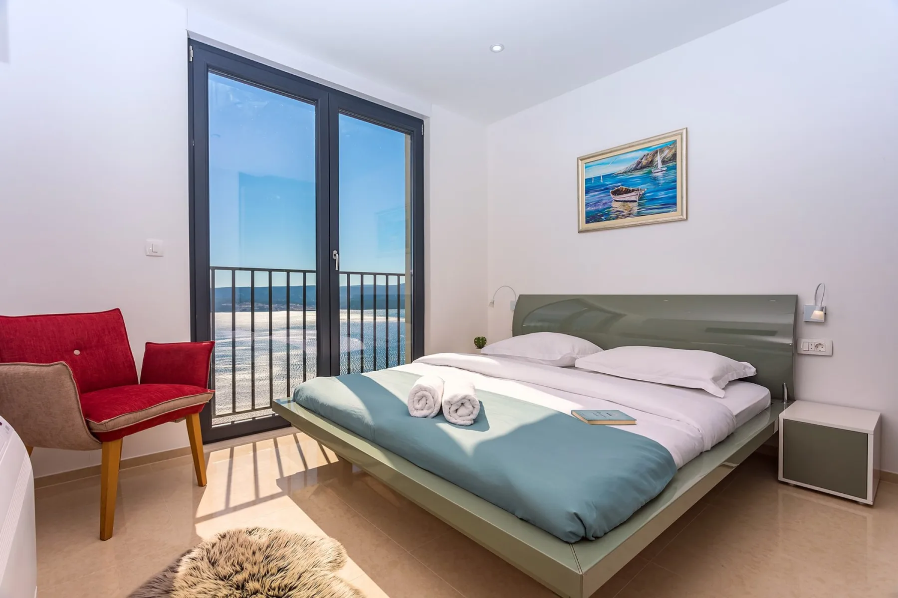 A bedroom with a bed beside tall glass doors opening onto a balcony.