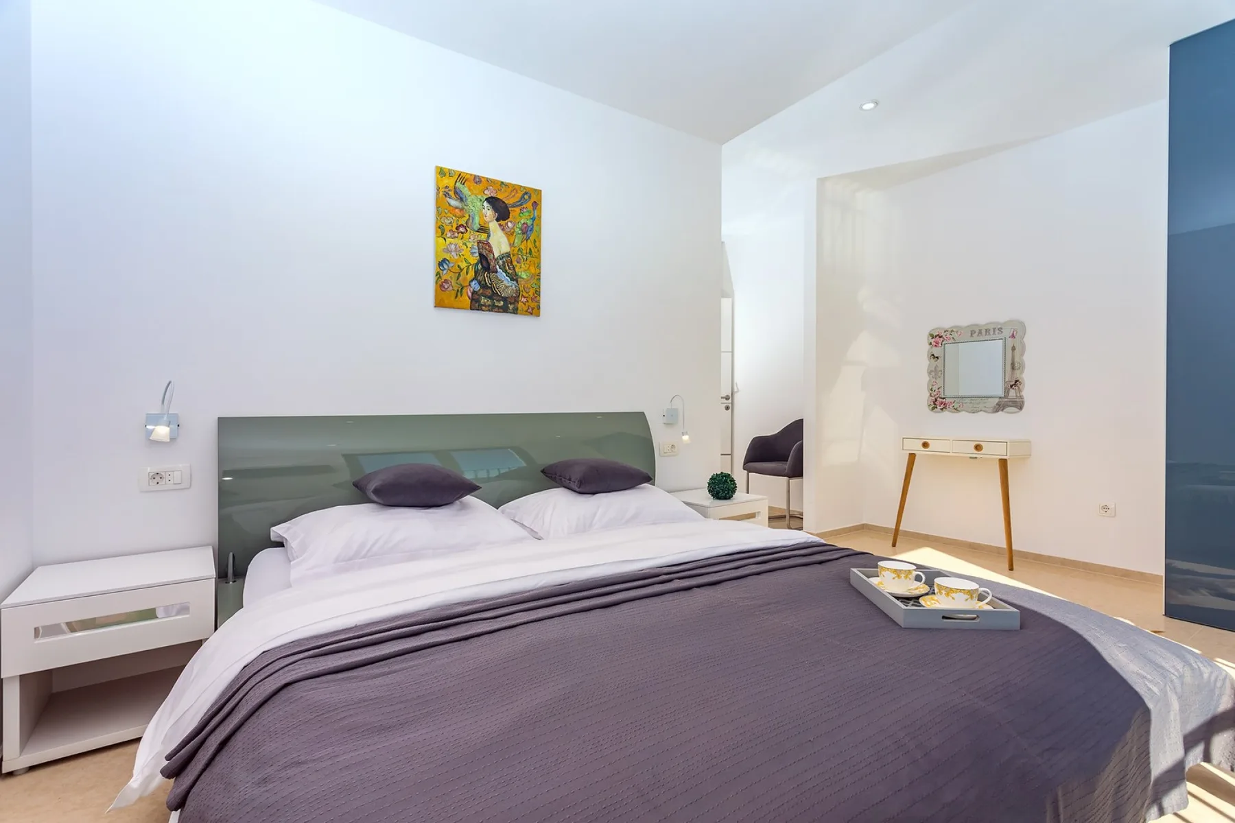 A bright bedroom with a neatly made bed and colorful wall art.