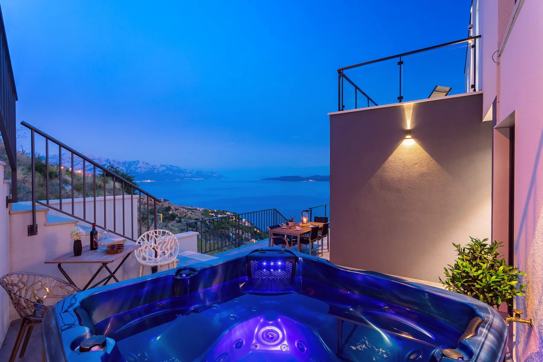 A rooftop terrace with a bubbling hot tub overlooking the sea at dusk.