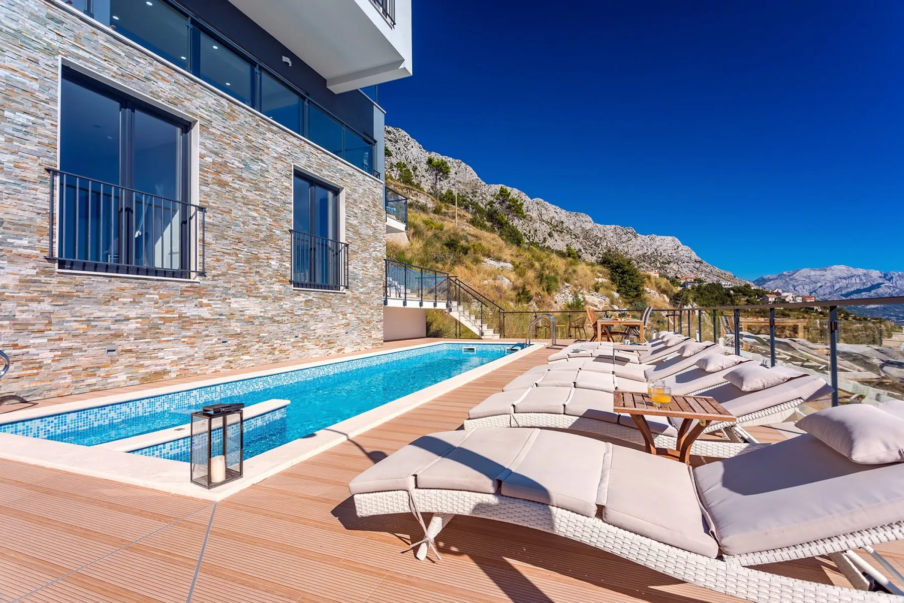 A poolside terrace with lounge seating overlooks a rocky hillside.