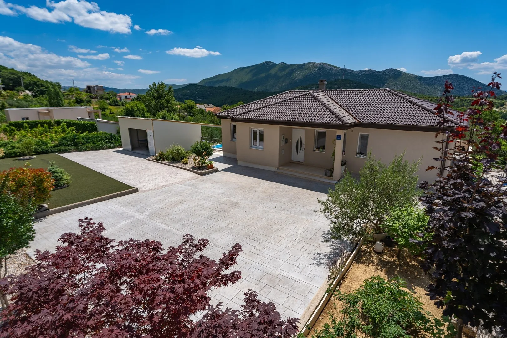 A single-story house faces a broad paved driveway, with mountains in the background.