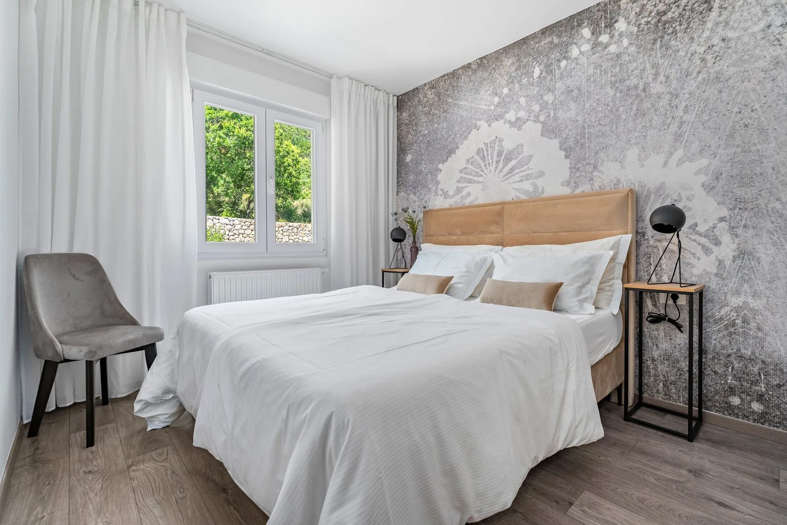 A bedroom with a neatly made bed beside a window and white curtains.