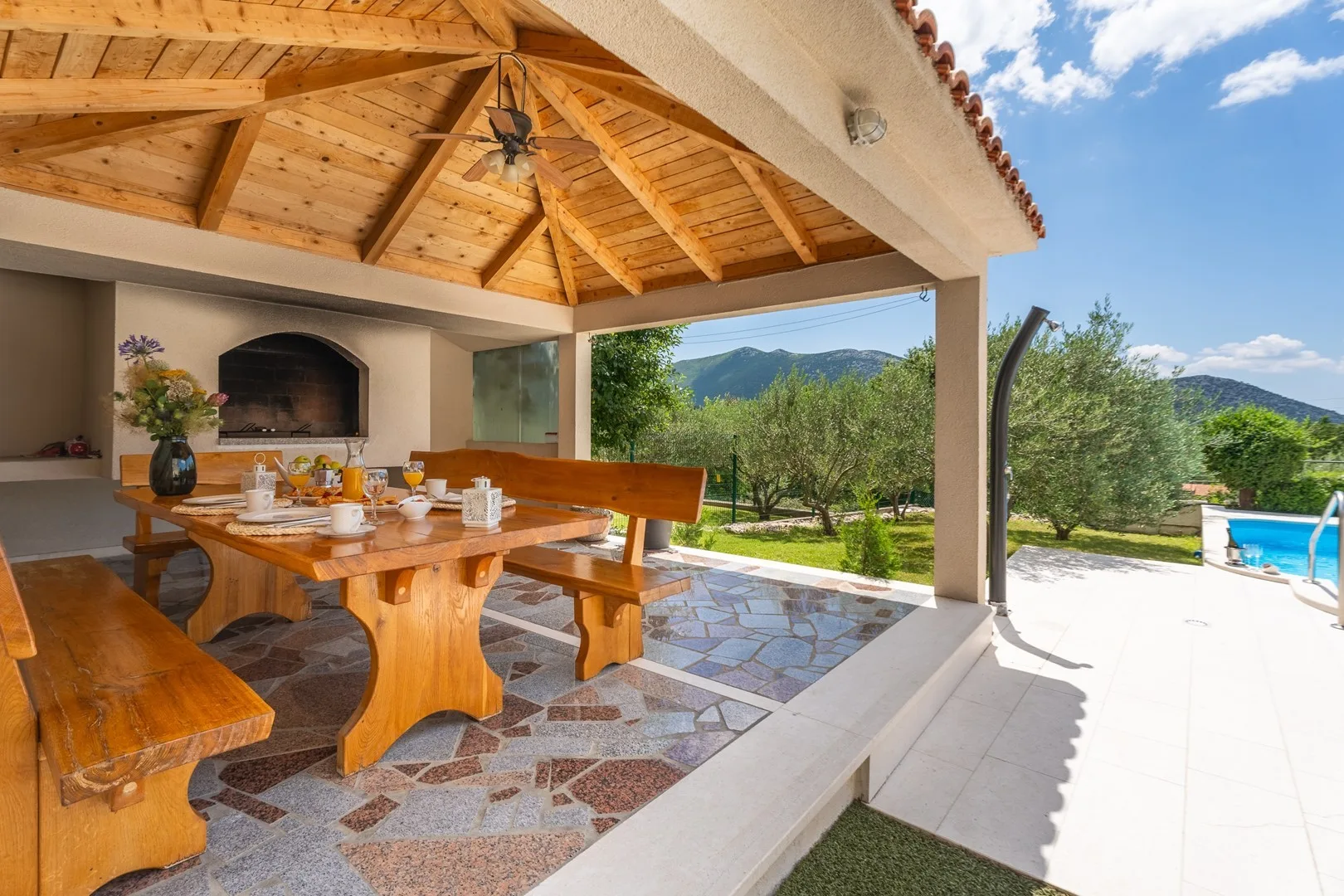 A covered outdoor dining area with a wooden table and mountain views.