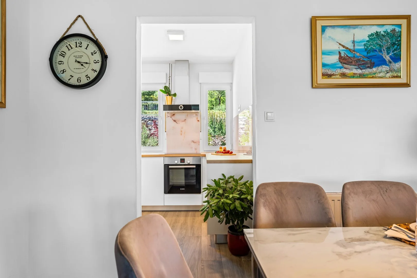 A dining area opens onto a bright kitchen with windows and a countertop.