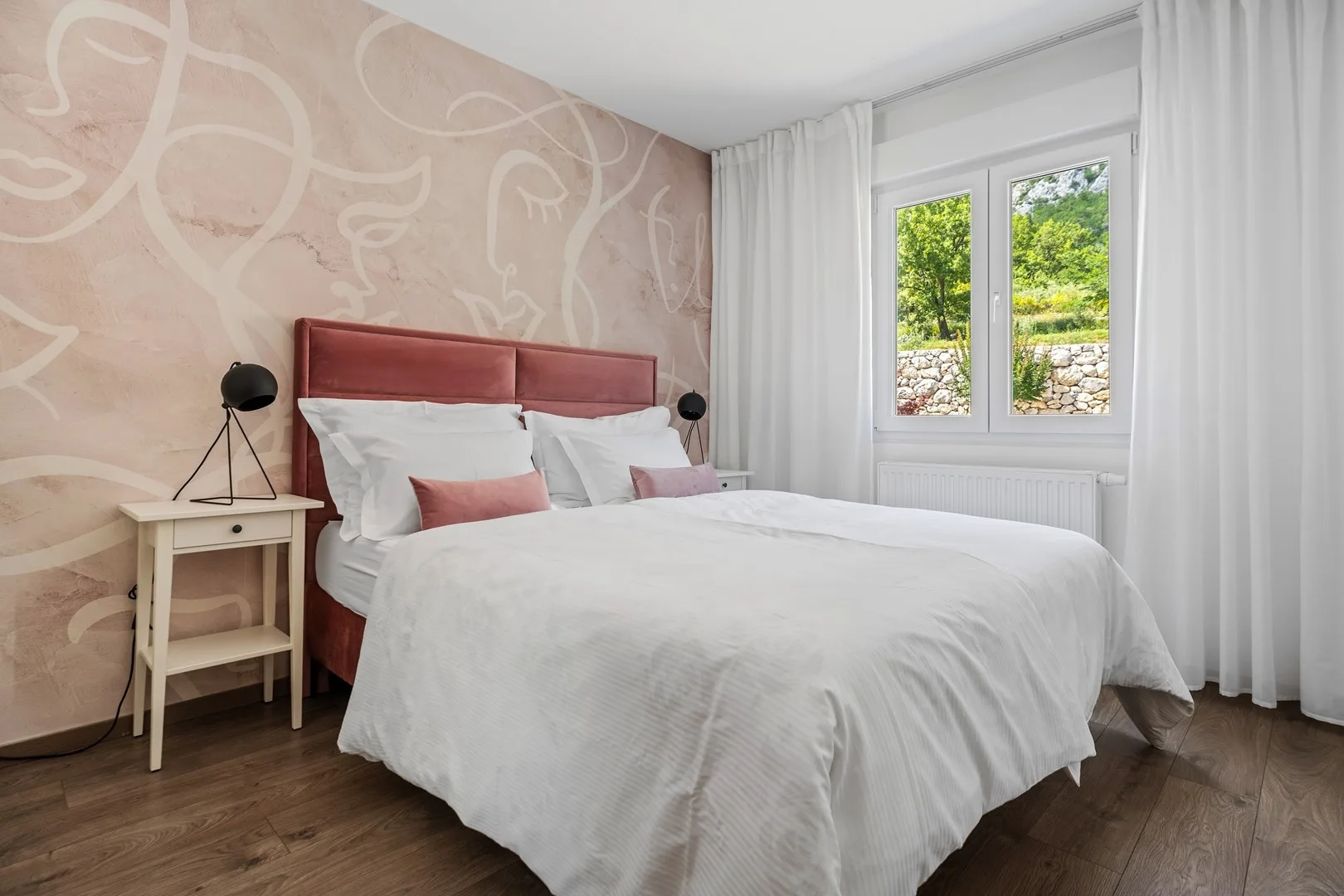 A bedroom with a bed beside a window framed by white curtains.