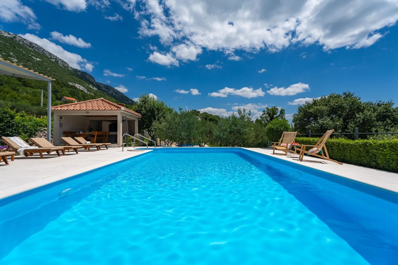 An outdoor swimming pool is surrounded by a paved deck and lounge seating.