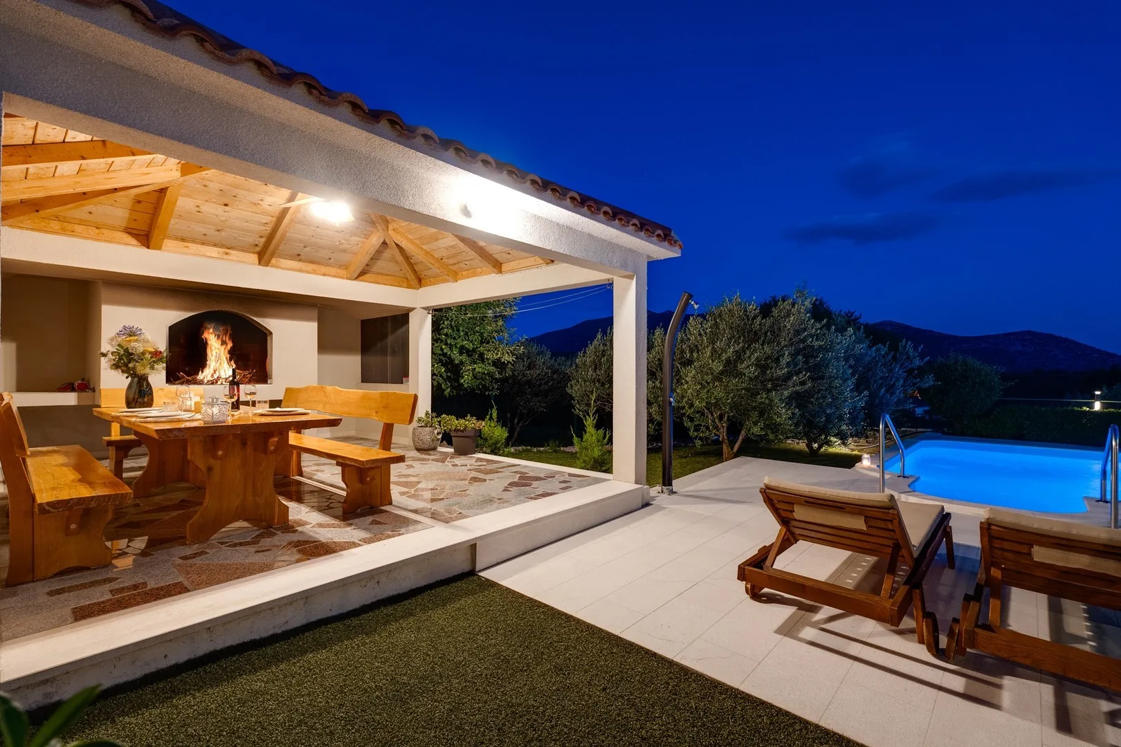 A covered outdoor dining area opens onto a patio beside a swimming pool.
