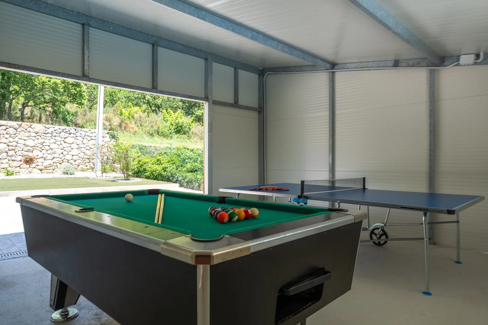 A covered recreation area with a green-felt pool table and a table tennis table.
