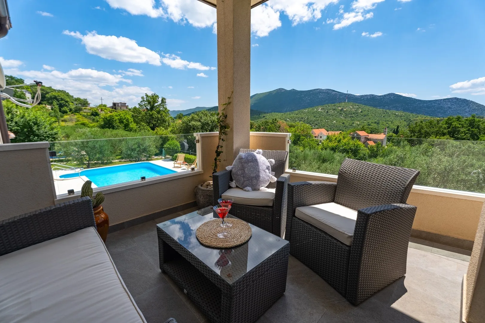 A covered outdoor seating area overlooks a swimming pool and green hills.