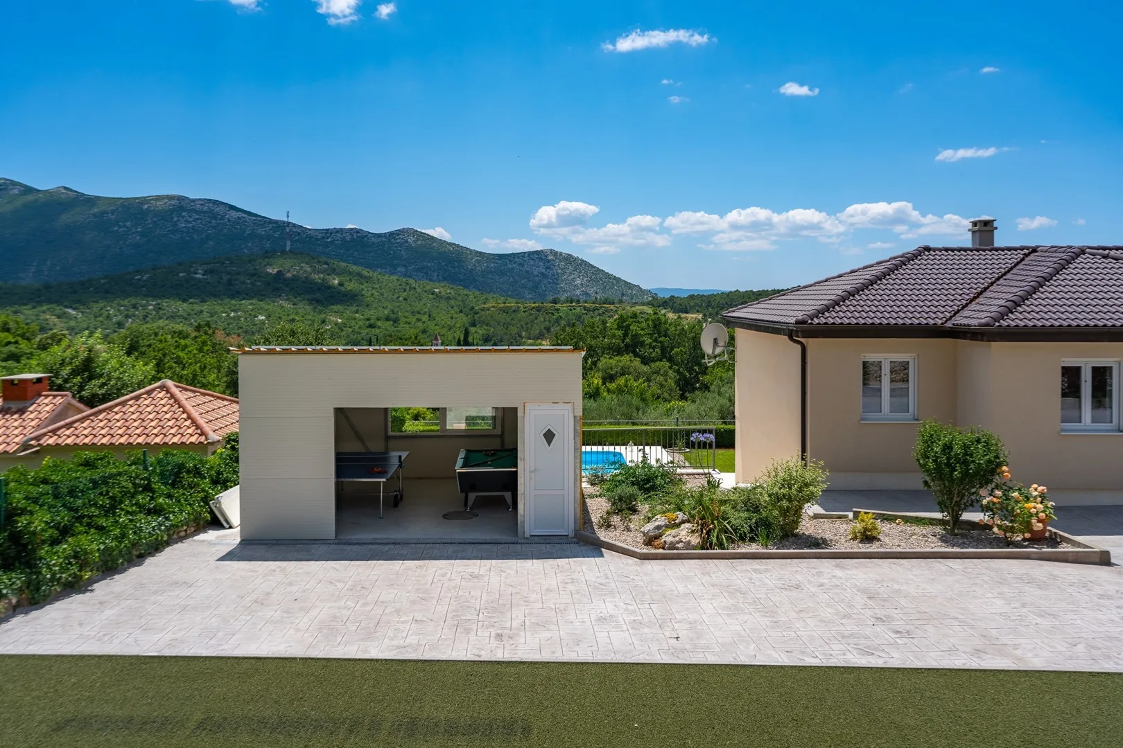 A paved outdoor area beside a small outbuilding, with green hills in the distance.