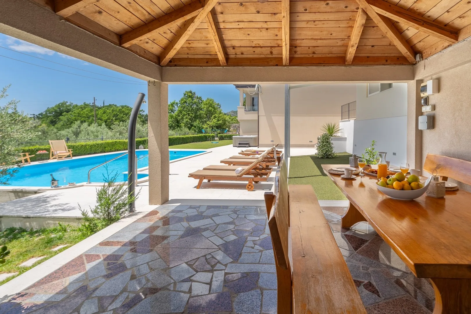 A covered patio overlooks a swimming pool, with outdoor seating and a dining table.