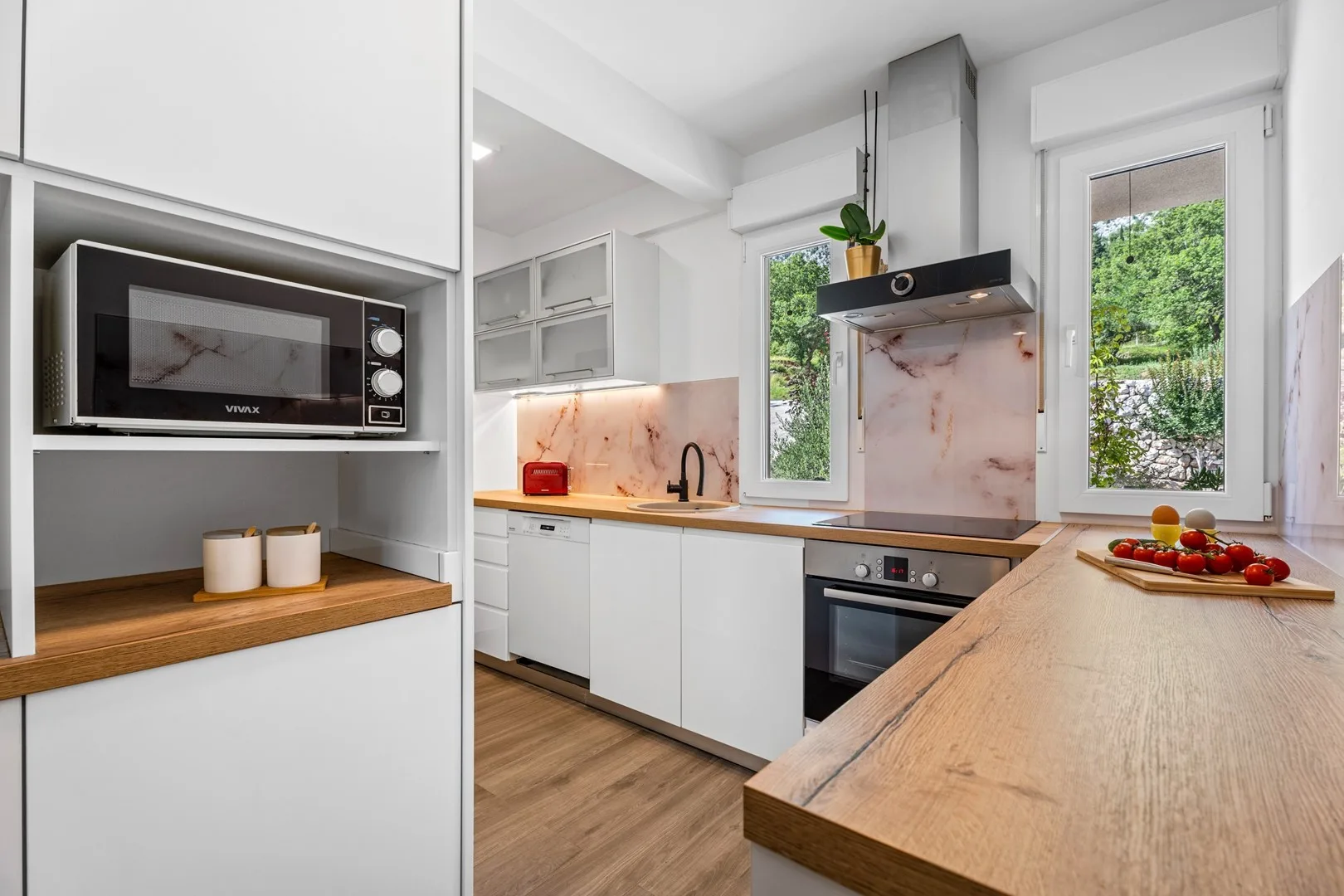 A bright kitchen with white cabinets, a cooktop, and a wood-topped island.