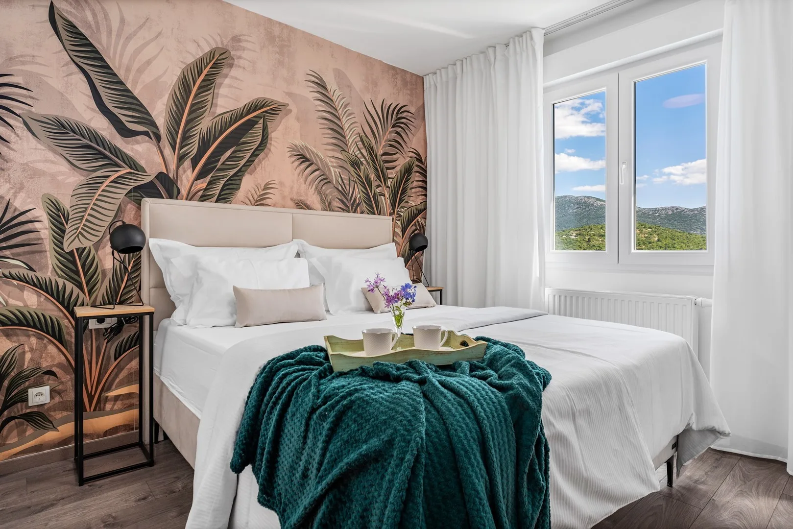 A bedroom with a neatly made bed and tropical leaf-patterned wallpaper.