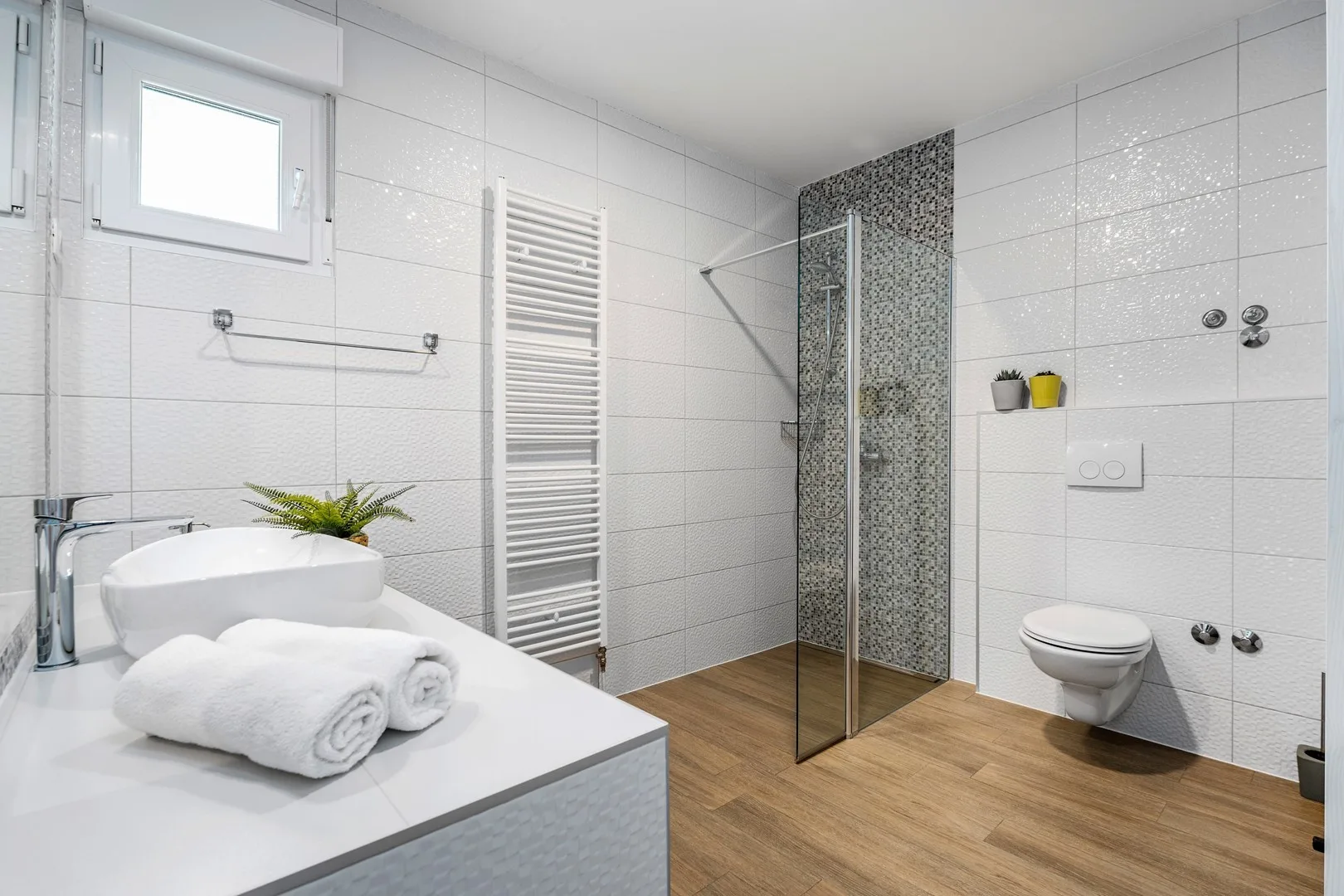 A bright tiled bathroom with a walk-in shower, toilet, and white sink.