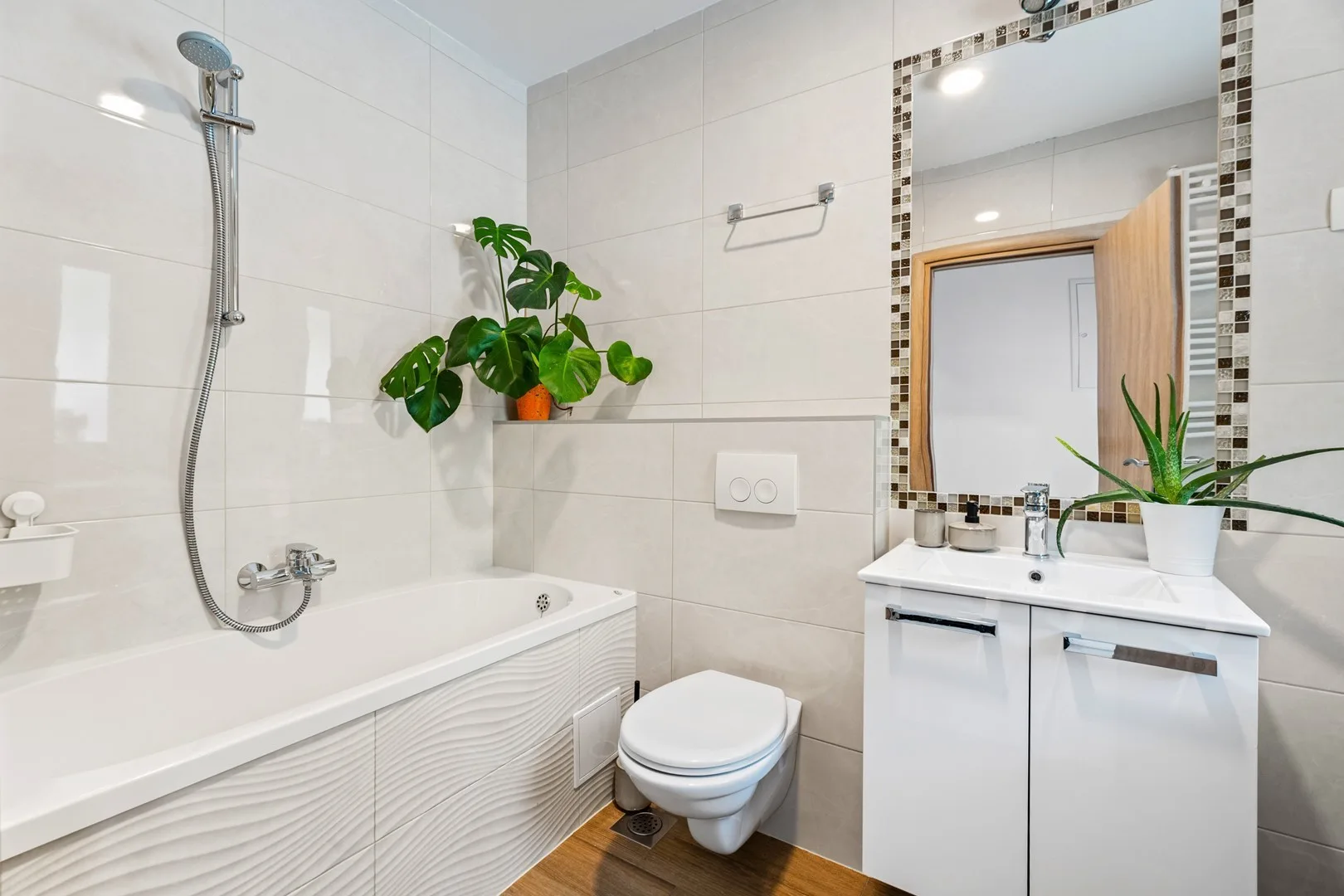 A bright tiled bathroom with a bathtub, toilet, and vanity.