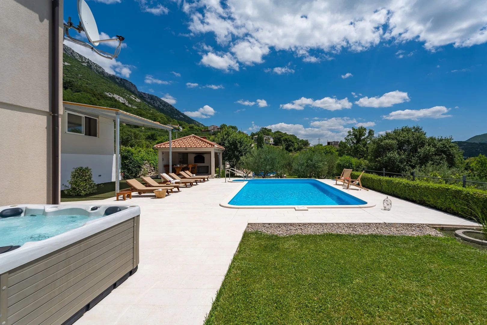 An outdoor pool area with a hot tub, loungers, and green lawn.